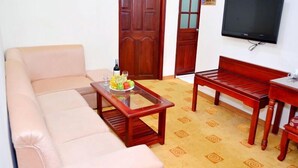 A living room with a sofa, a coffee table with fruit, a wooden bench, and a TV on the wall. - Asia Hotel Can Tho (Can Tho)