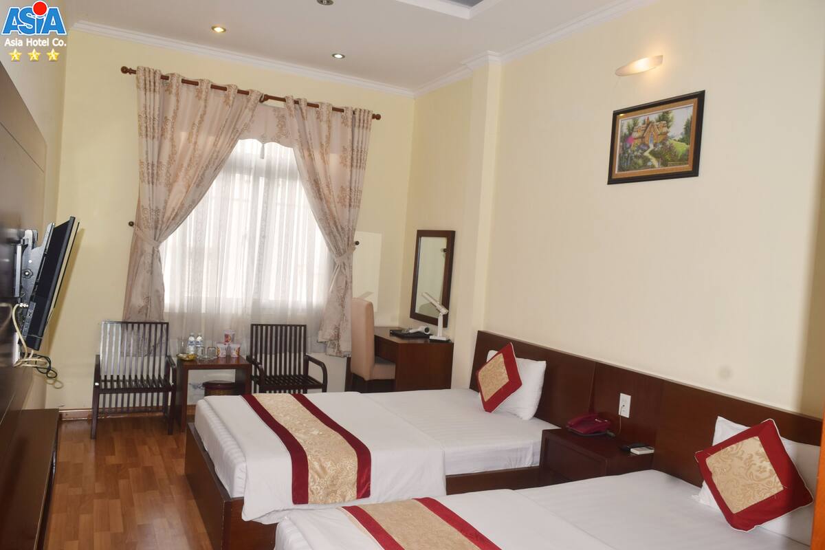 A hotel room with two beds, a desk, a chair, a television, and a painting on the wall.