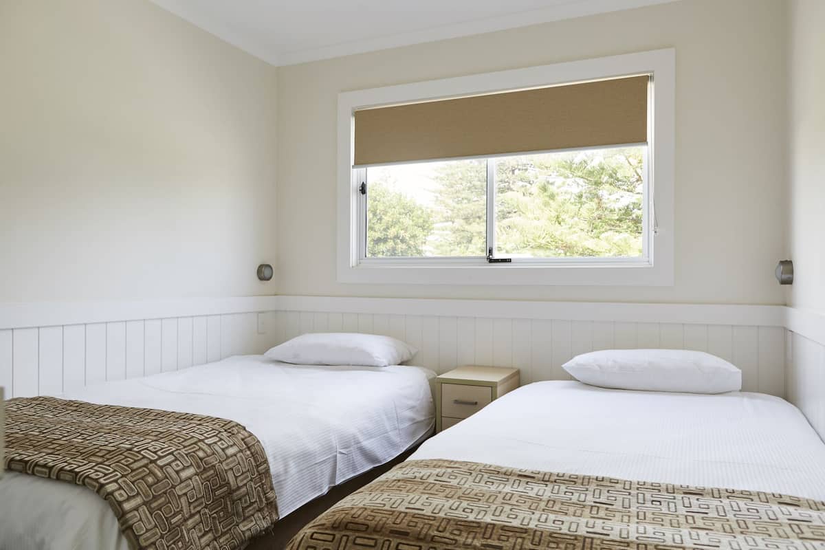 Une chambre avec deux lits, une fenêtre donnant sur un paysage verdoyant et un mur blanc.