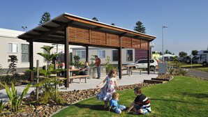 An outdoor seating area with tables and benches, surrounded by a landscaped garden with rocks and plants. - NRMA Stockton Beach Holiday Park (Stockton)