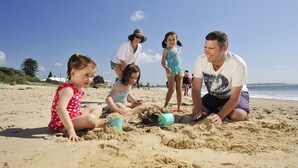 A family on a sandy beach with a clear sky. - NRMA Stockton Beach Holiday Park (Stockton)