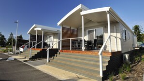 A modern mobile home with a covered porch, a staircase leading to the entrance, and a small outdoor seating area. - NRMA Stockton Beach Holiday Park (Stockton)