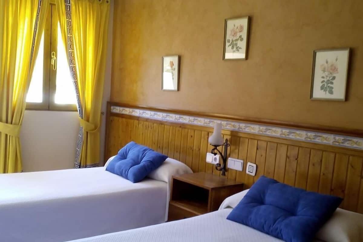 A hotel room with two beds, yellow curtains, wooden paneling, and floral wall art.