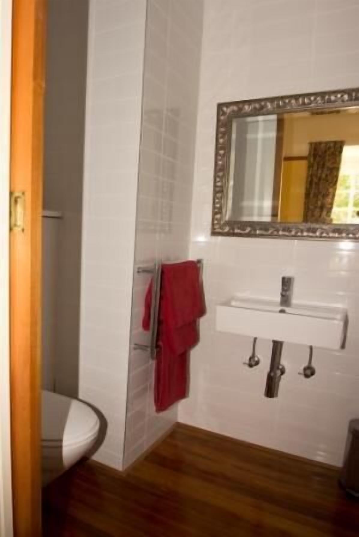Un baño con un lavamanos blanco, un espejo y una toalla roja colgada en un perchero.