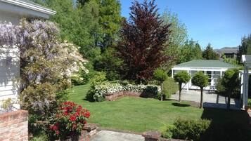 Un giardino curato con prato, diverse piante fiorite e un vialetto in mattoni che conduce a un patio coperto.