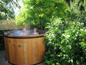 A wooden hot tub with two people inside, surrounded by lush greenery. - Cheltenham House (Hanmer Springs)