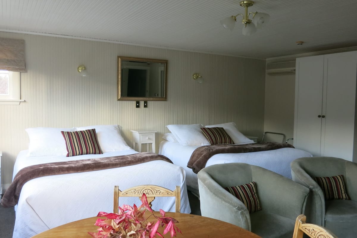 Quarto de hotel com duas camas, uma mesa com um vaso e uma cadeira.