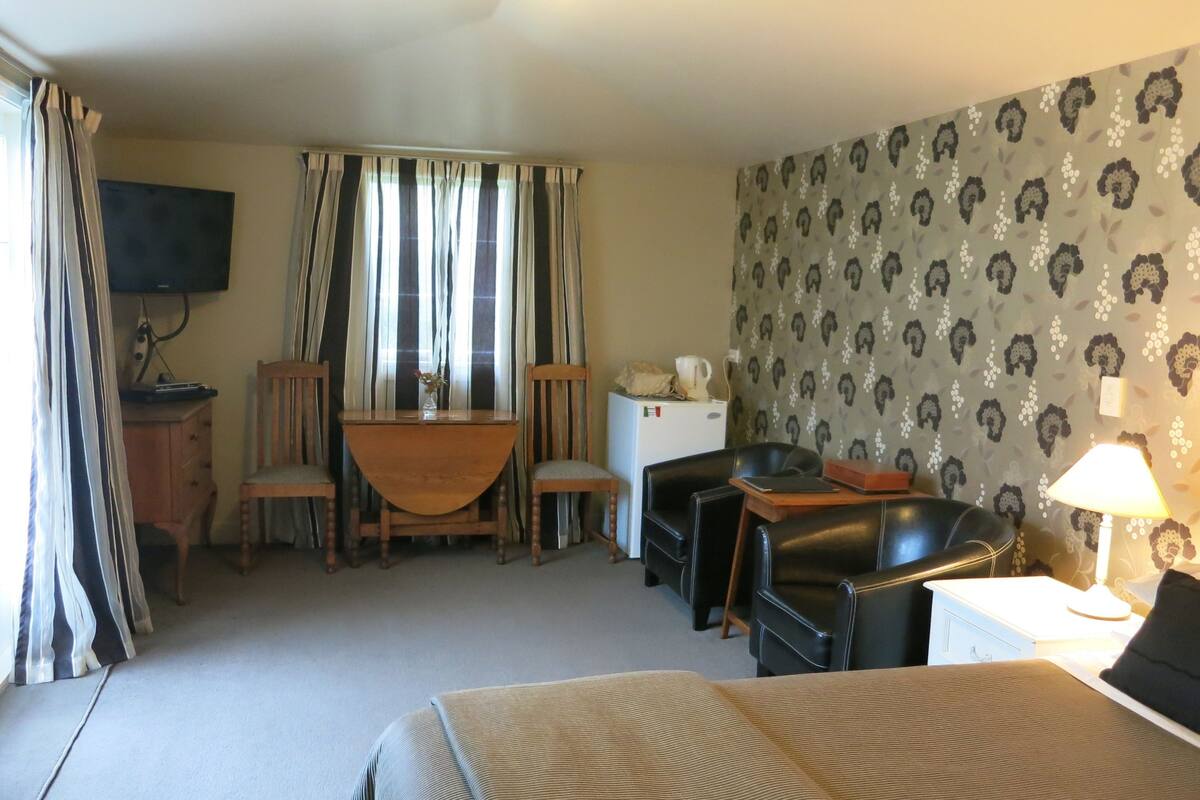Quarto de hotel com cama, escrivaninha com cadeira, televisão, frigorífico e candeeiro.