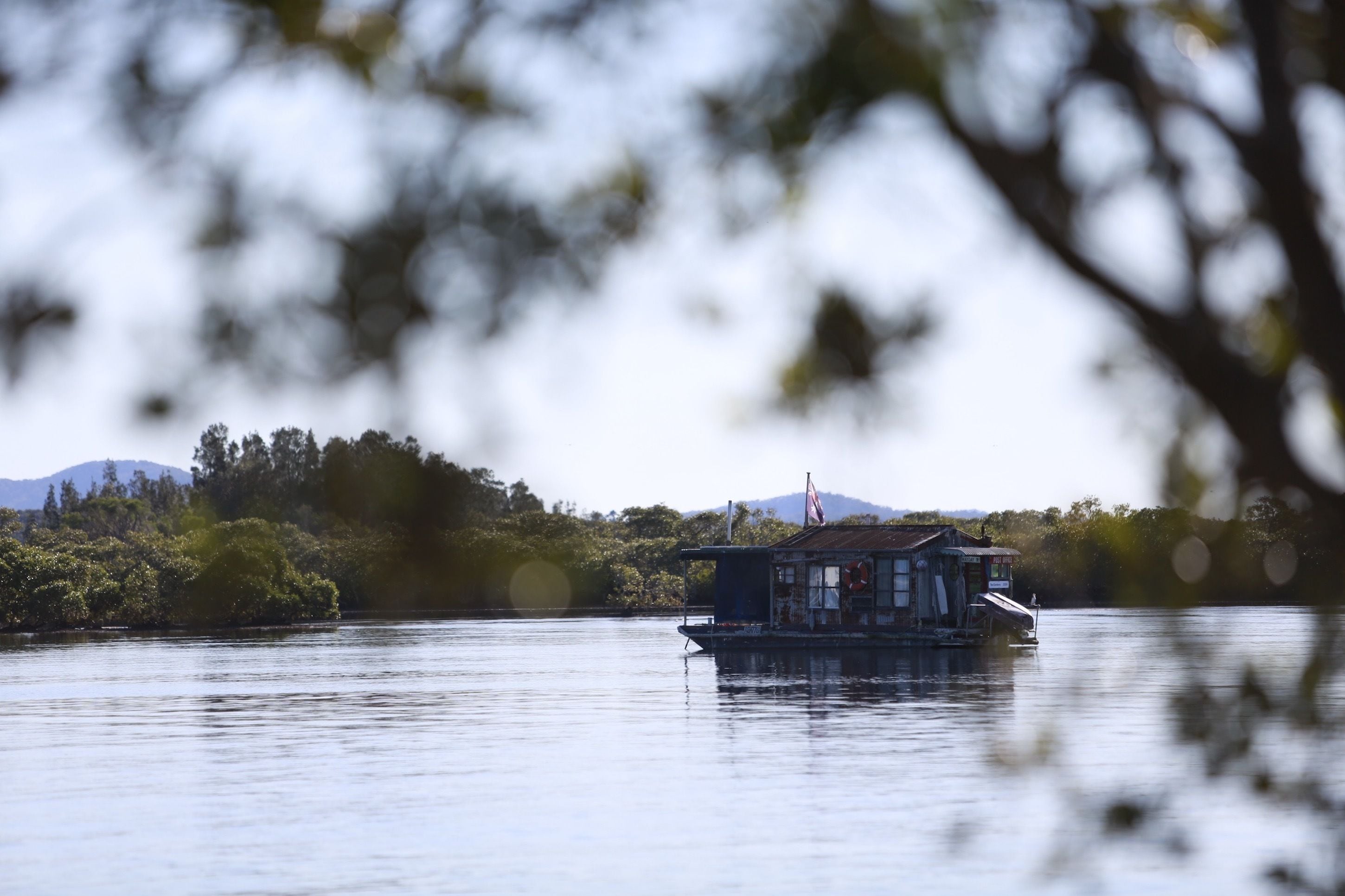 A houseboat on a calm lake with a forested shoreline and mountains in the background.