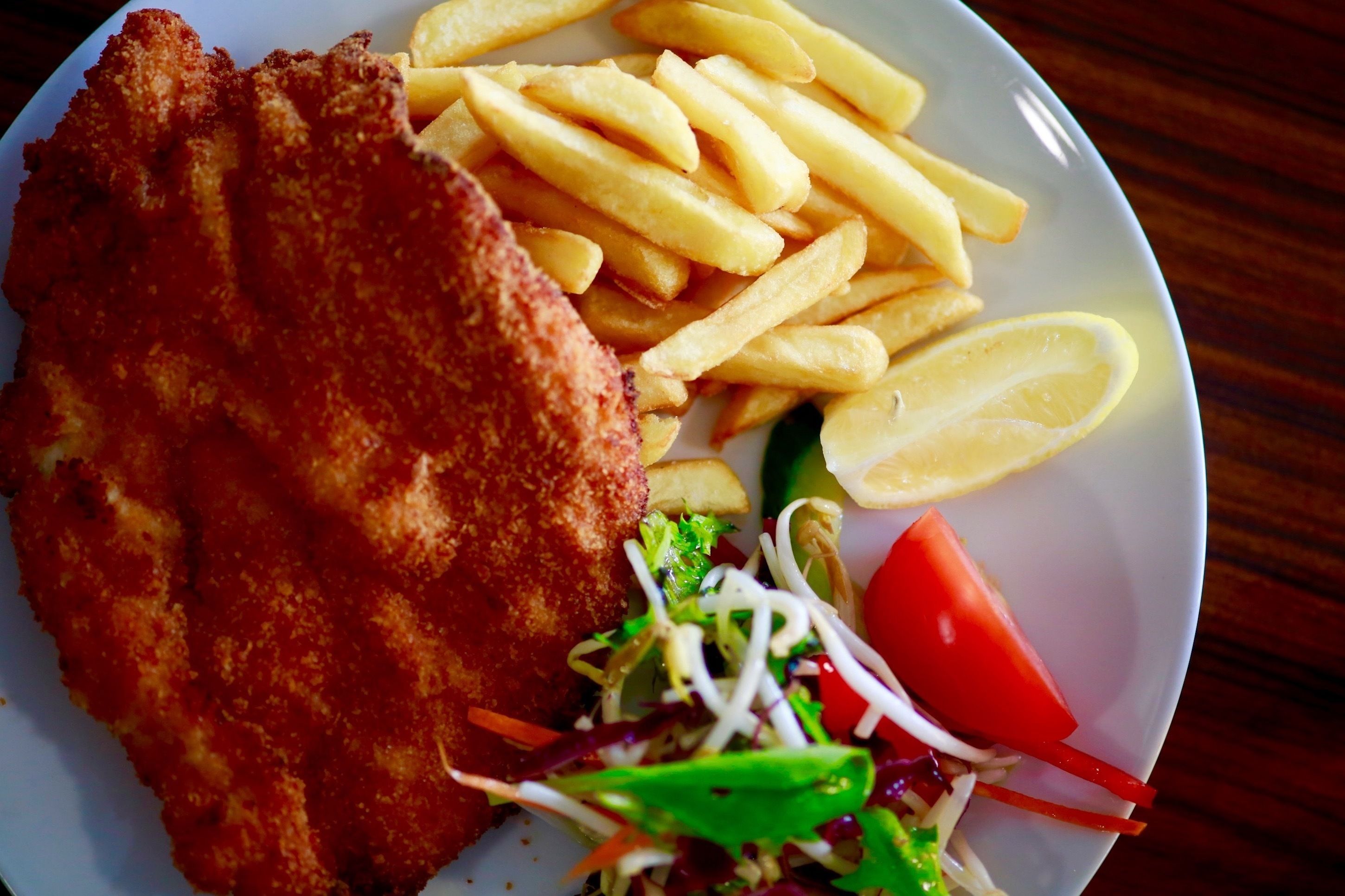 A plate with a breaded cutlet, French fries, a lemon wedge, and a salad.