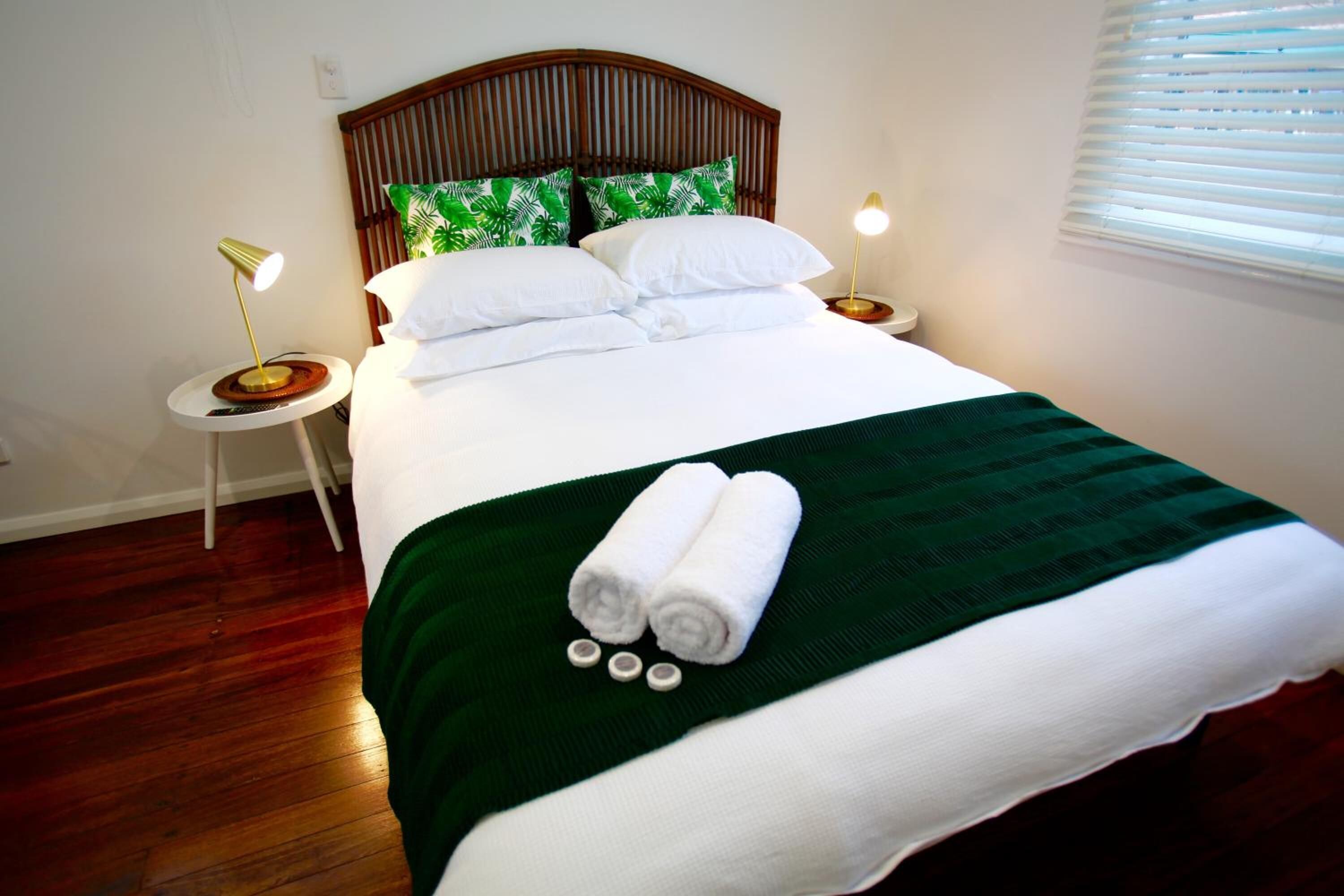 A neatly made bed with white linens, a green throw blanket, and rolled towels. There are two bedside tables with lamps.
