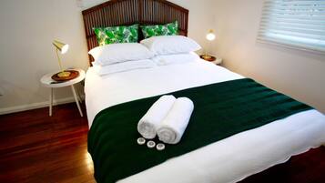 A neatly made bed with white linens, a green throw blanket, and rolled towels. There are two bedside tables with lamps.