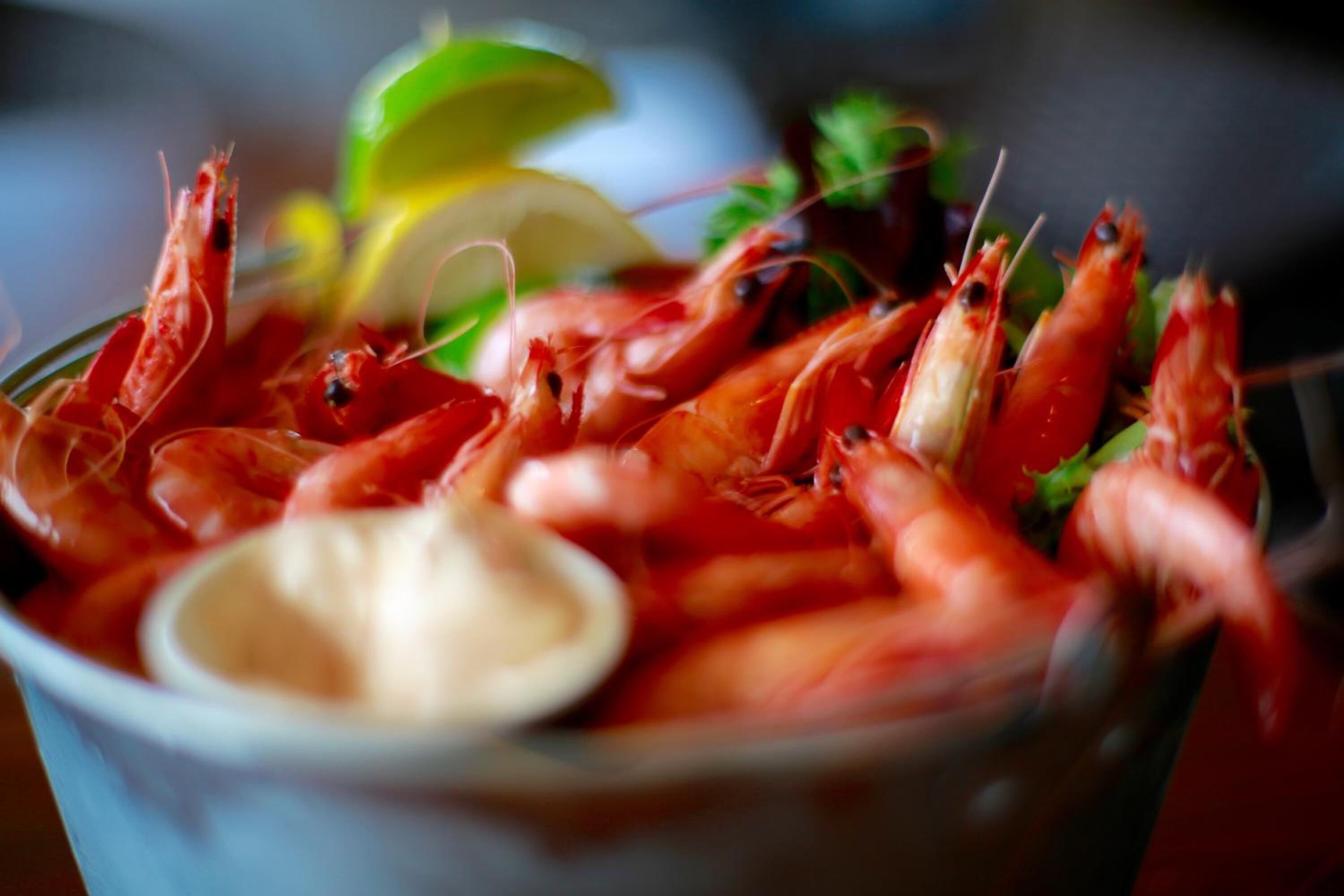 A bowl of cooked shrimp with a side of dipping sauce and a slice of lime.