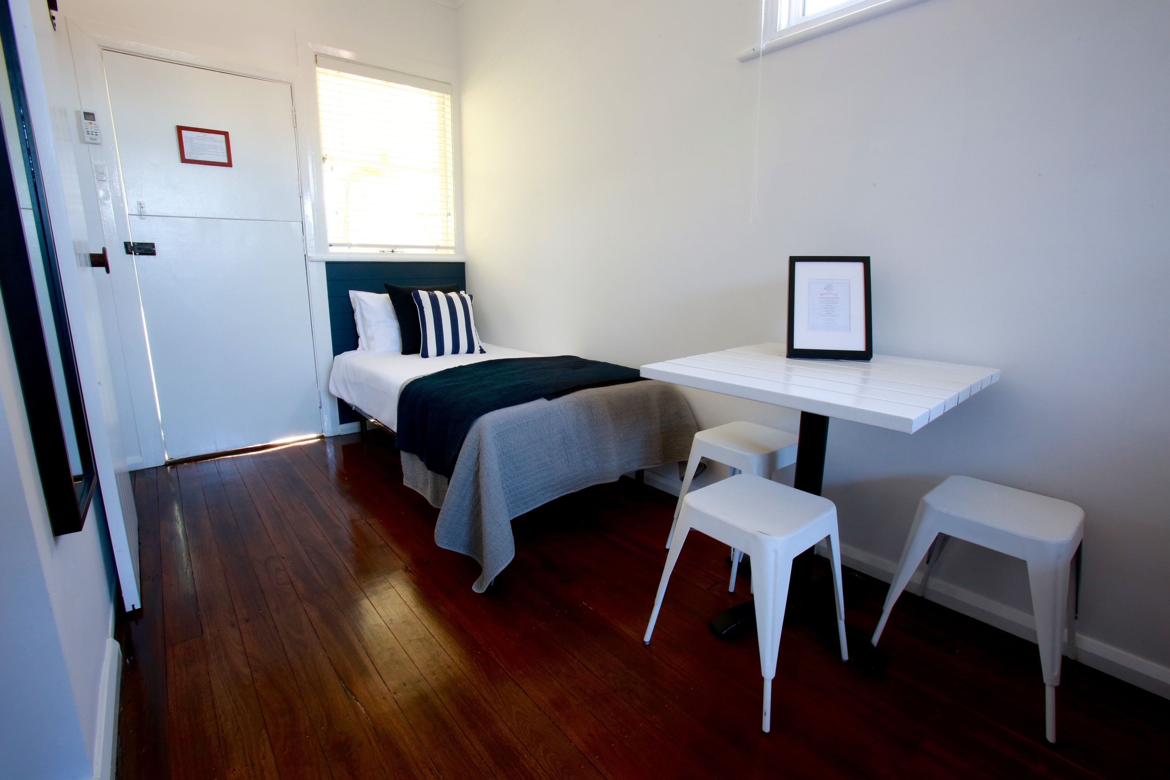 Een kleine, schone kamer met een bed, een bureau en twee witte krukken.