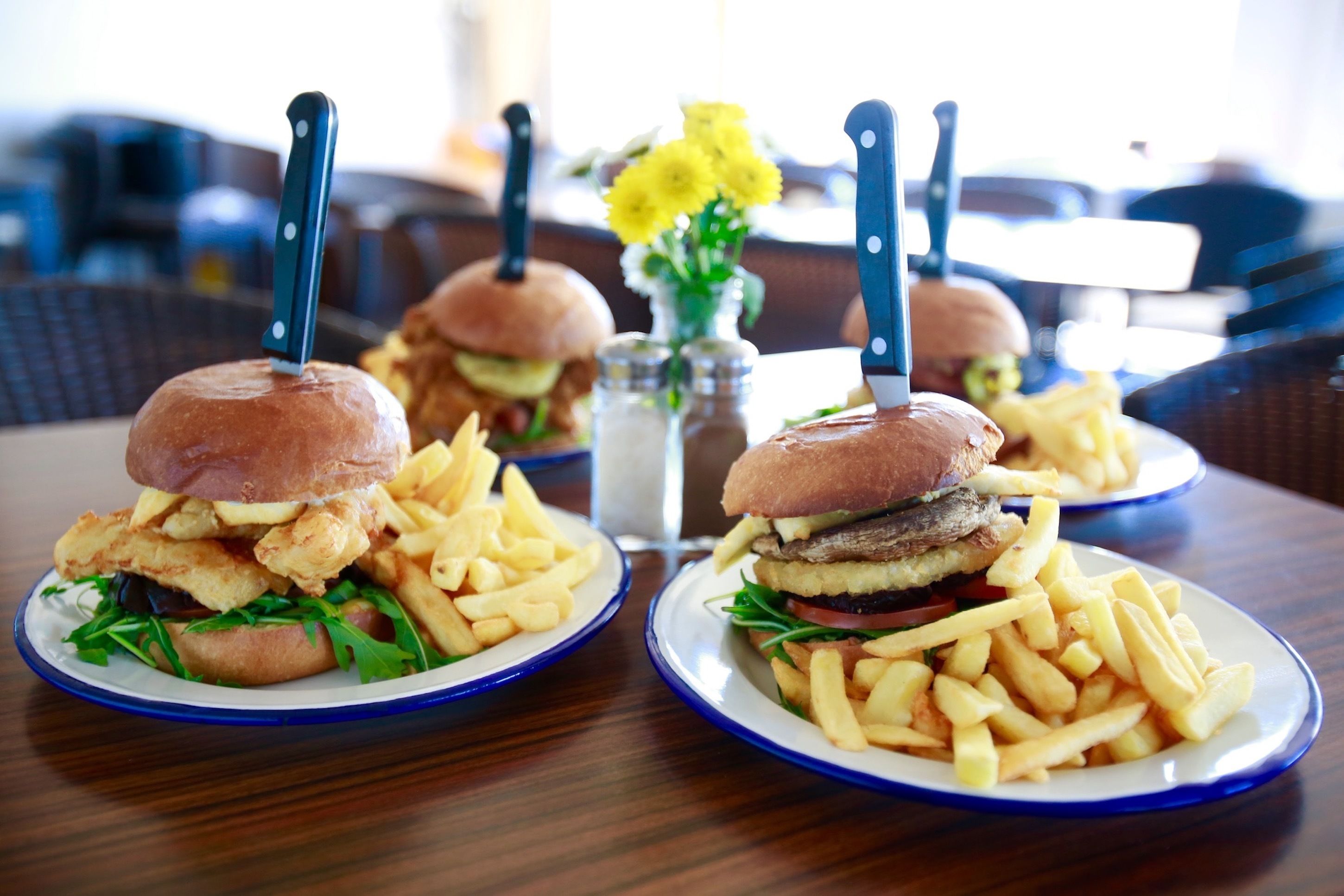 Une table avec deux assiettes de nourriture, chacune contenant un hamburger et des frites, ainsi qu’un salier et un poivrier.