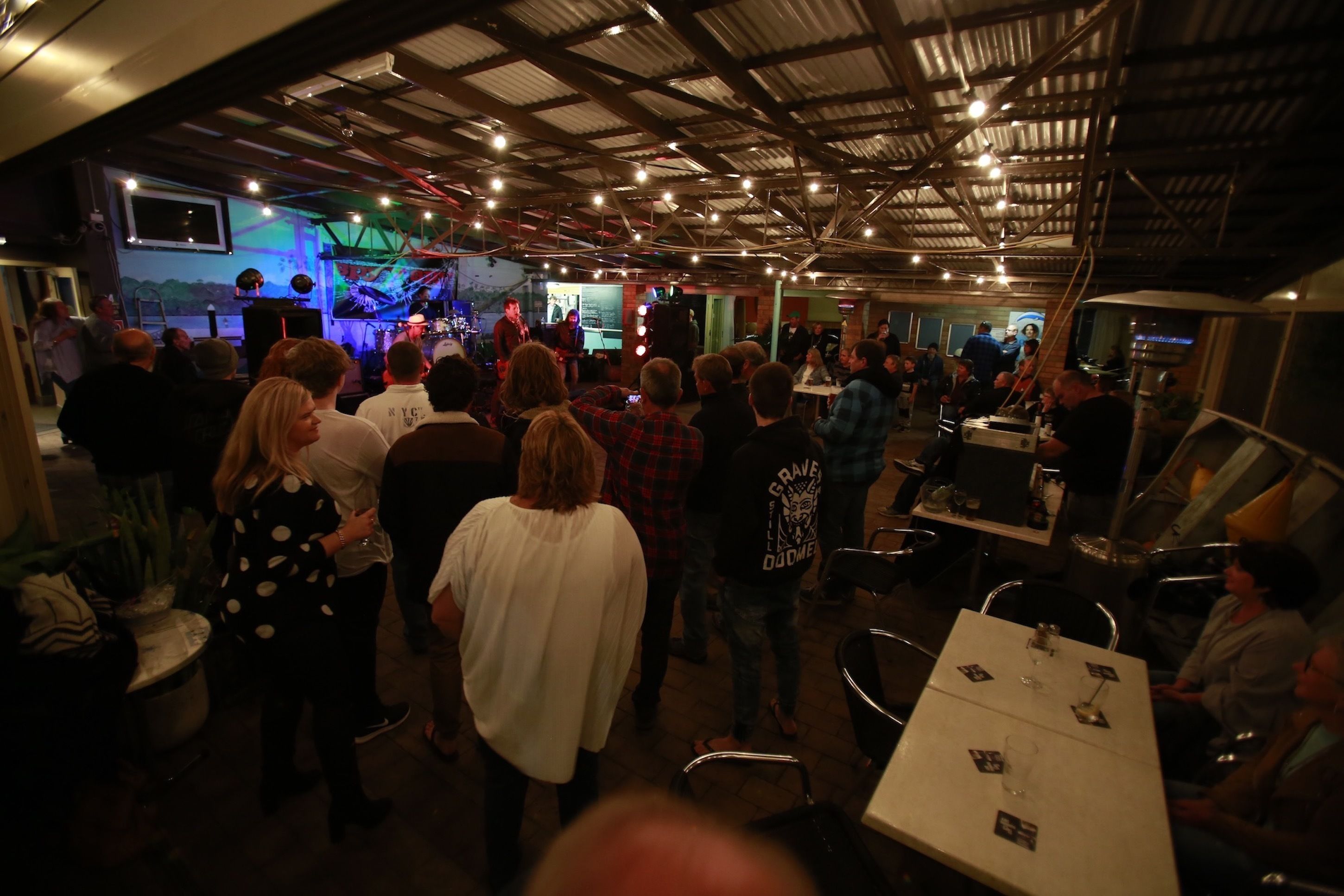 A crowded indoor event space with a stage, tables, and chairs.