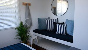Un dormitorio moderno con una cama blanca, un espejo redondo y una toalla a rayas negras y blancas sobre un perchero de madera.