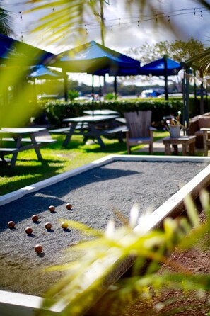 A shuffleboard table with pucks, a blue canopy, and picnic tables in a sunny outdoor setting. - Tea Gardens Hotel (Tea Gardens)