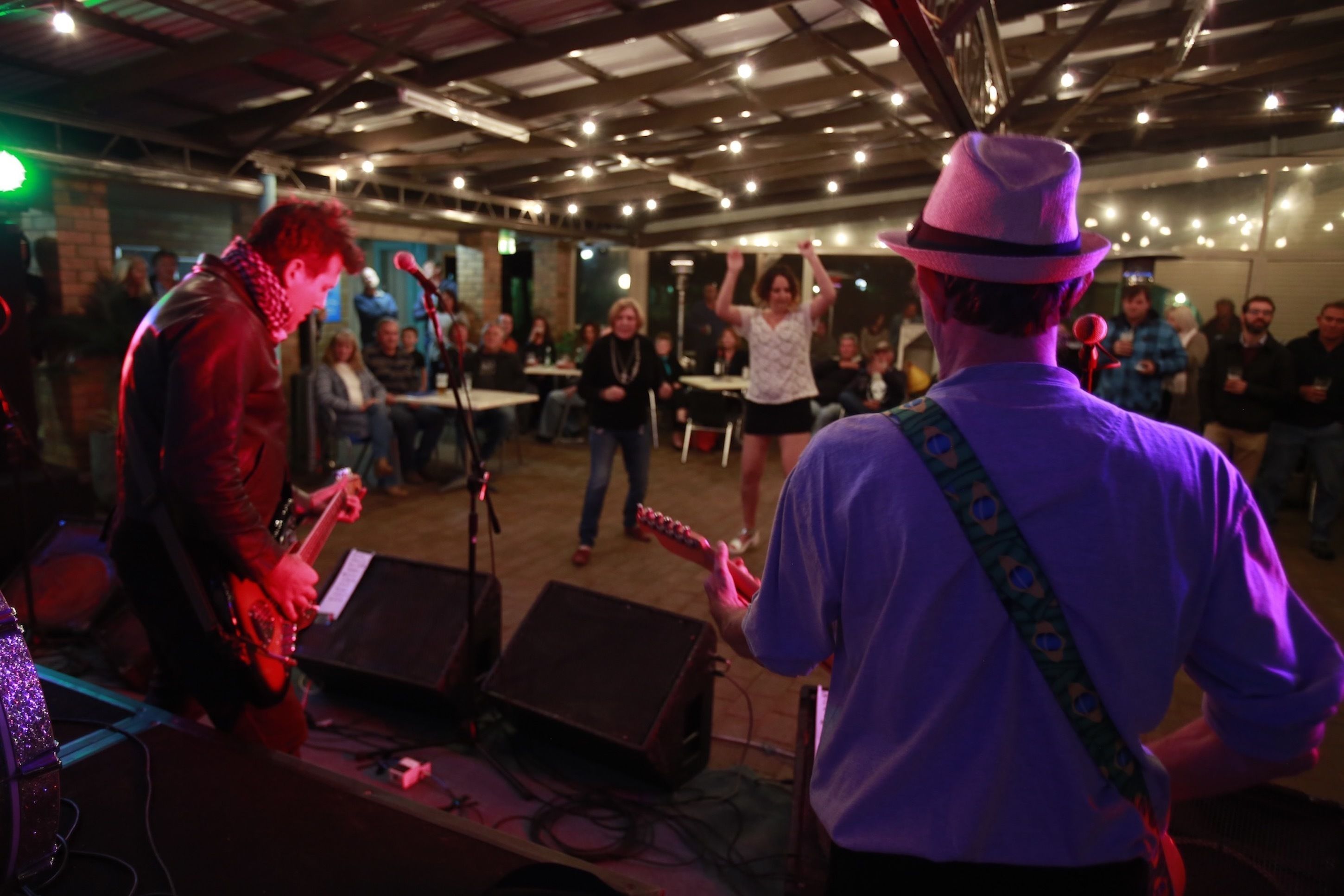 A band performing in a venue with a rustic ceiling and tables set up for an audience.