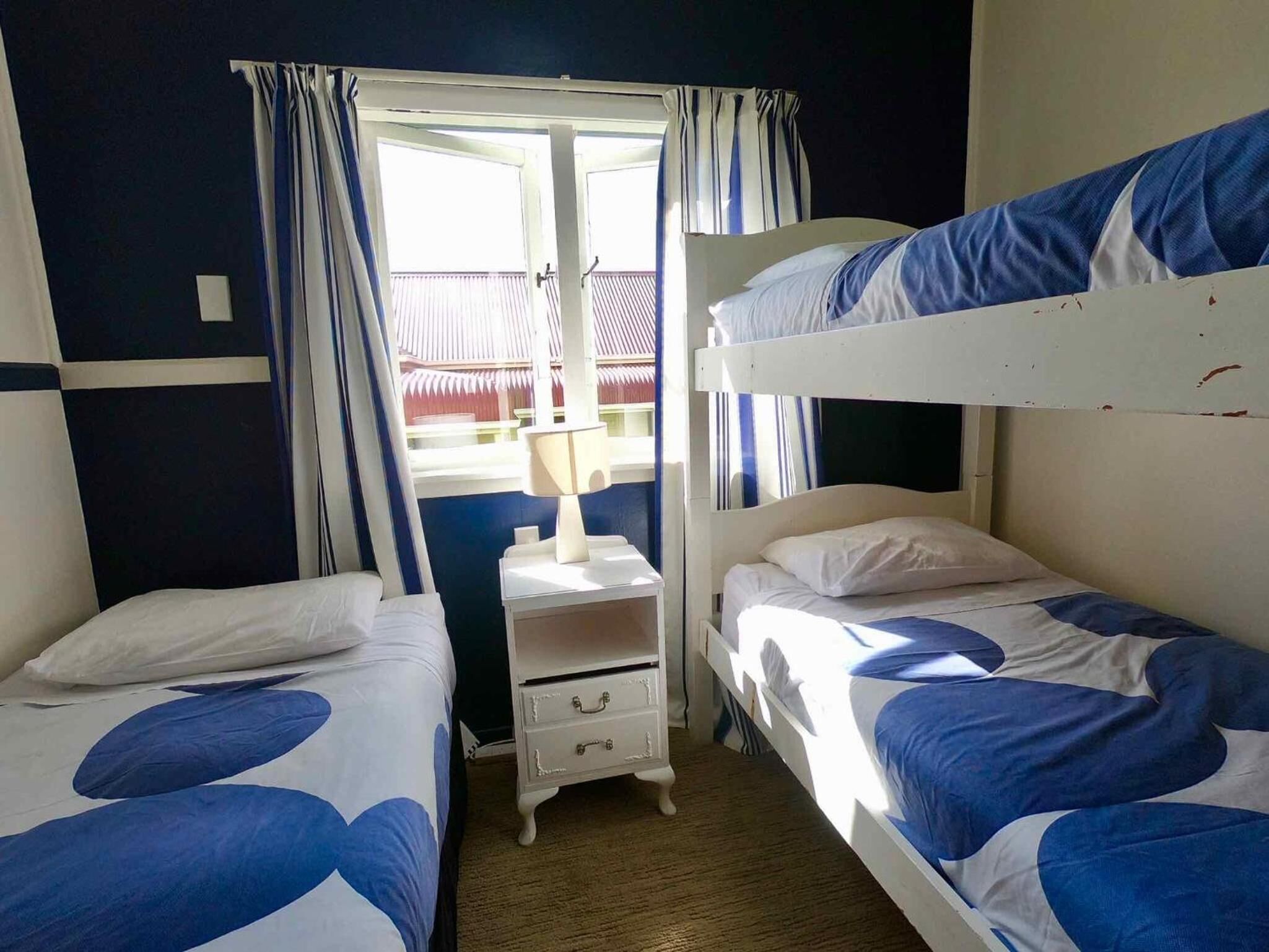 A room with two bunk beds, a bedside table with a lamp, and a window with curtains.