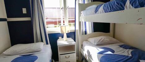 A room with two bunk beds, a bedside table with a lamp, and a window with curtains.
