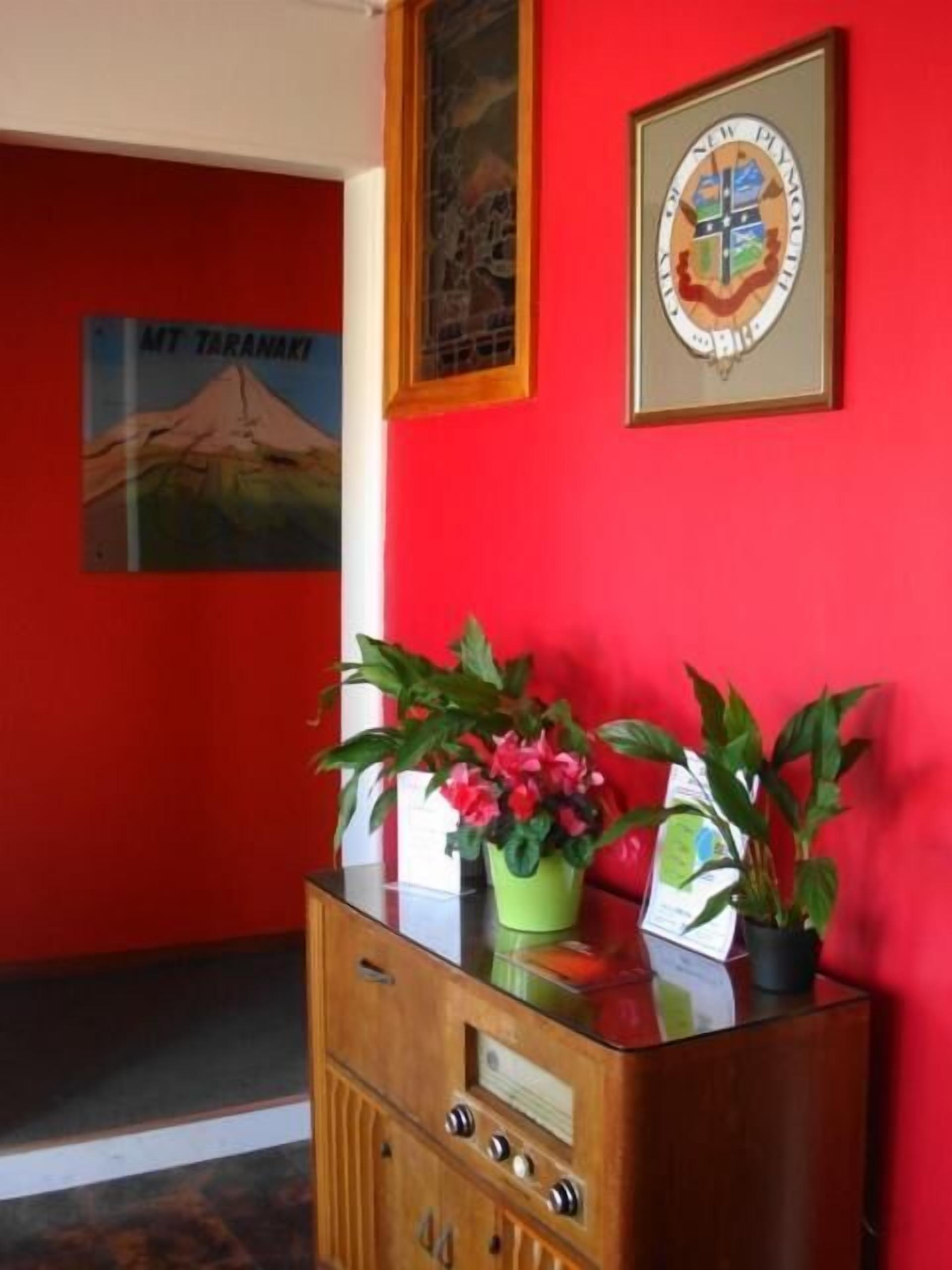 Una habitación con paredes rojas, un aparador de madera, un escudo enmarco y un cartel de Monte Taranaki.