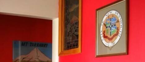 Una habitación con paredes rojas, un aparador de madera, un escudo enmarco y un cartel de Monte Taranaki.