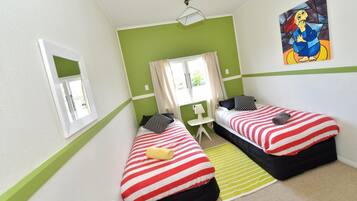 Una habitación con dos camas, una mesita, una silla y una ventana con cortinas.