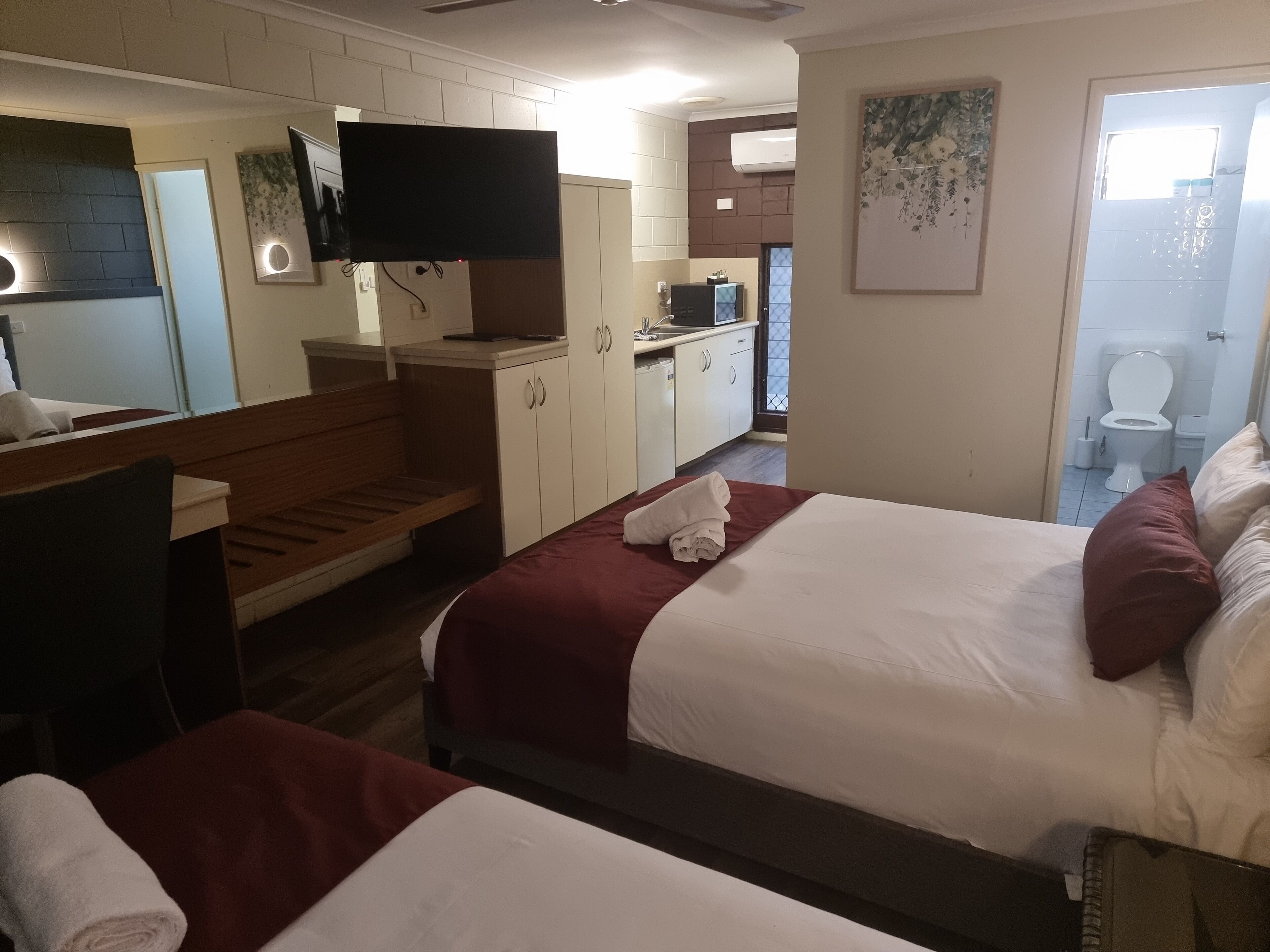 A hotel room with two beds, a TV, a bathroom, and a kitchenette.
