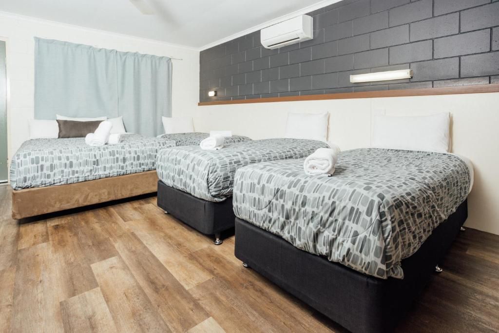 Ein Hotelzimmer mit zwei Betten, Holzboden, einer Ziegelwand und einer Klimaanlage.