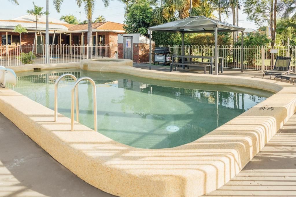 Une piscine entourée d’une terrasse, un espace de repos couvert et une zone délimitée par une clôture.