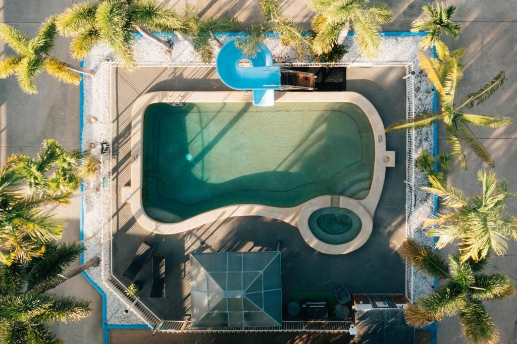 Vista aérea de un área de piscina con palmeras, un tobogán de agua y una zona para tomar el sol.