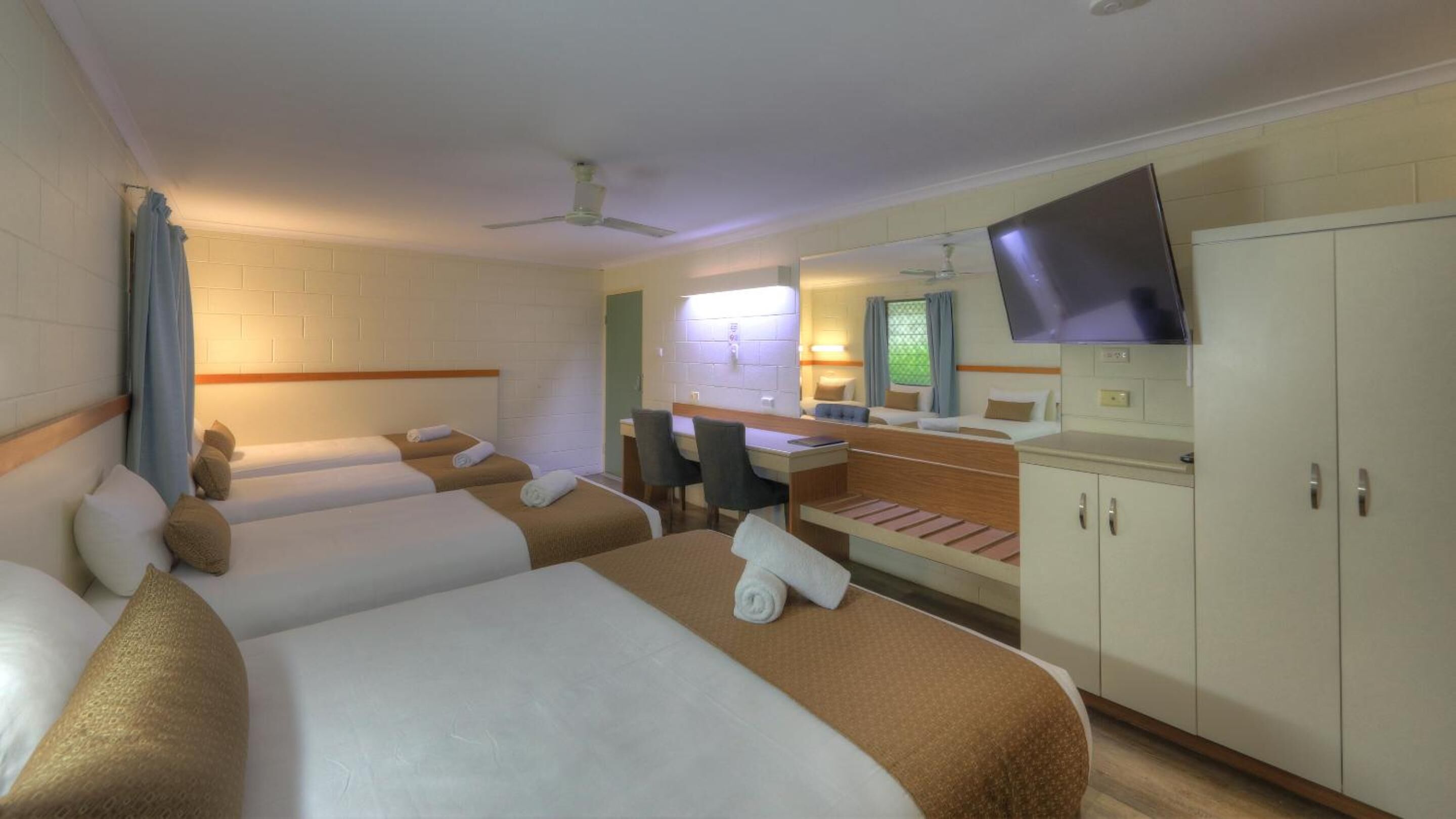 Habitación de hotel con tres camas, un escritorio, un televisor y un armario.