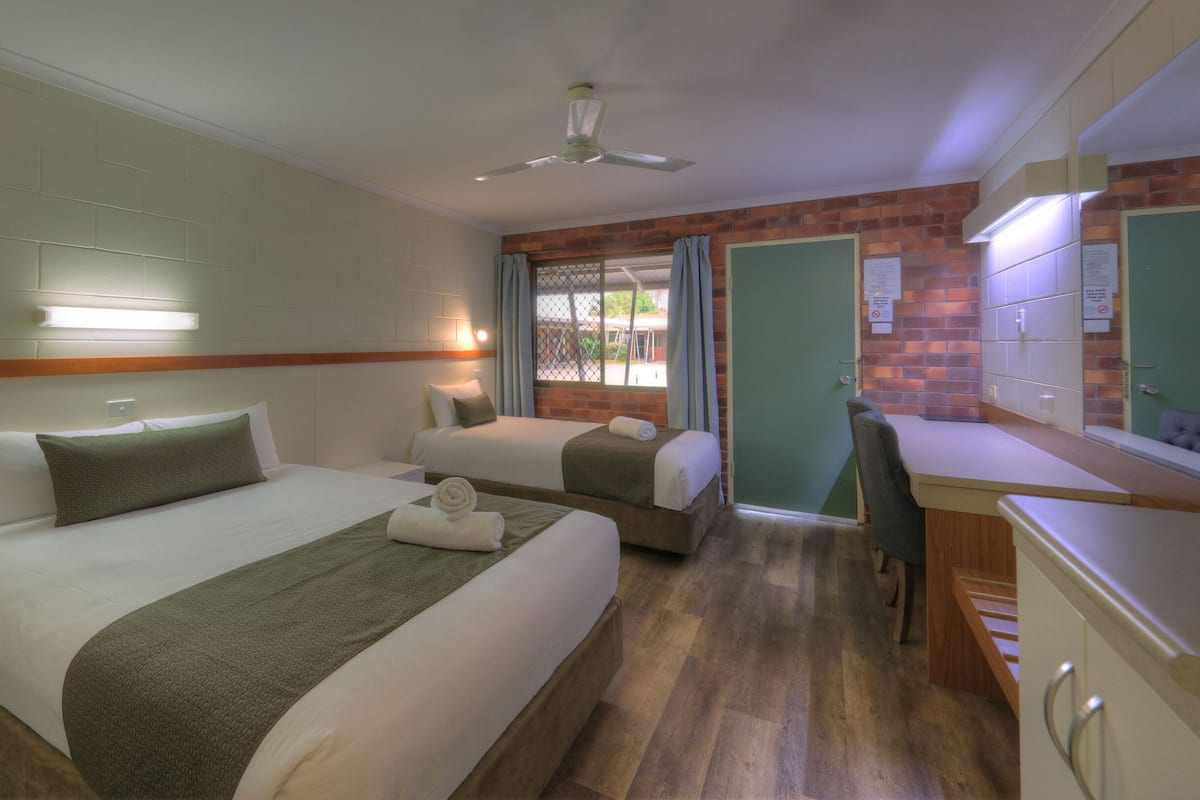Une chambre d’hôtel avec deux lits, un bureau, une chaise, un ventilateur de plafond et un mur en briques.