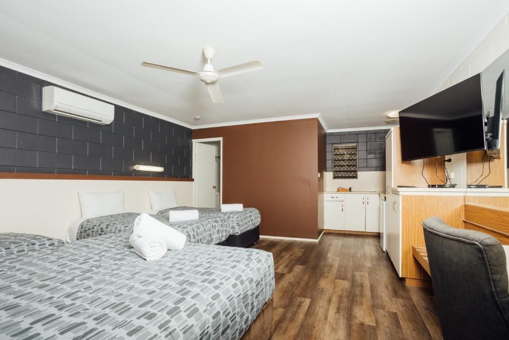 Habitació d'hotel amb dos llits, una petita cuina, un televisor i un ventilador de sostre.