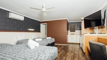 Habitació d'hotel amb dos llits, una petita cuina, un televisor i un ventilador de sostre.