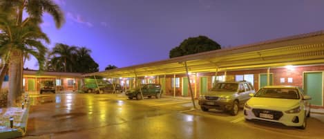 Un motel con área de estacionamiento techada, varias habitaciones y una palmera en primer plano.