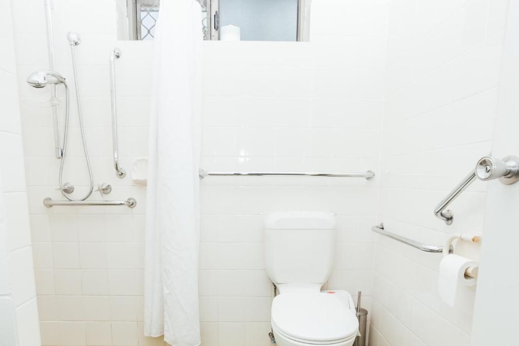 A bathroom with a white toilet, a shower with a handheld showerhead, and grab bars.