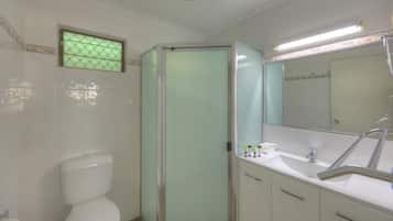 A bathroom with a toilet, a glass-enclosed shower, a sink with a mirror, and toiletries on the counter.
