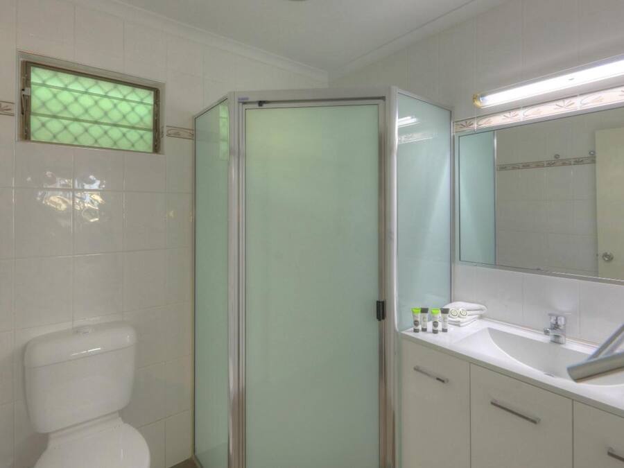 A bathroom with a toilet, a glass-enclosed shower, a sink with a mirror, and toiletries on the counter.