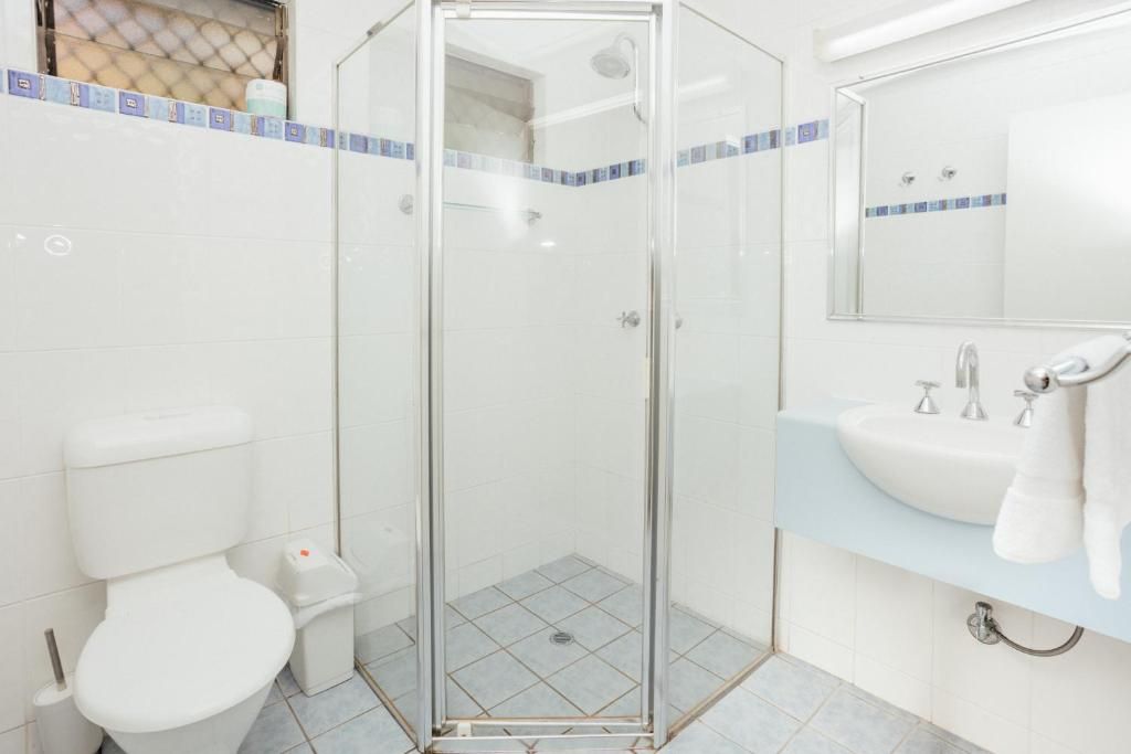 A bathroom with a glass-enclosed shower, a white toilet, and a sink with a mirror above it.