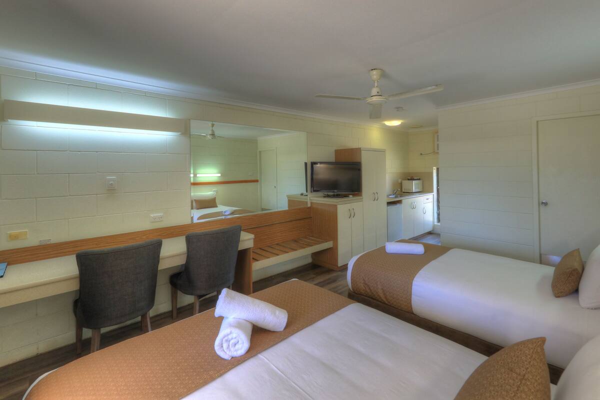 Une chambre d’hôtel avec deux lits, un bureau, une chaise, une télévision et une kitchenette.