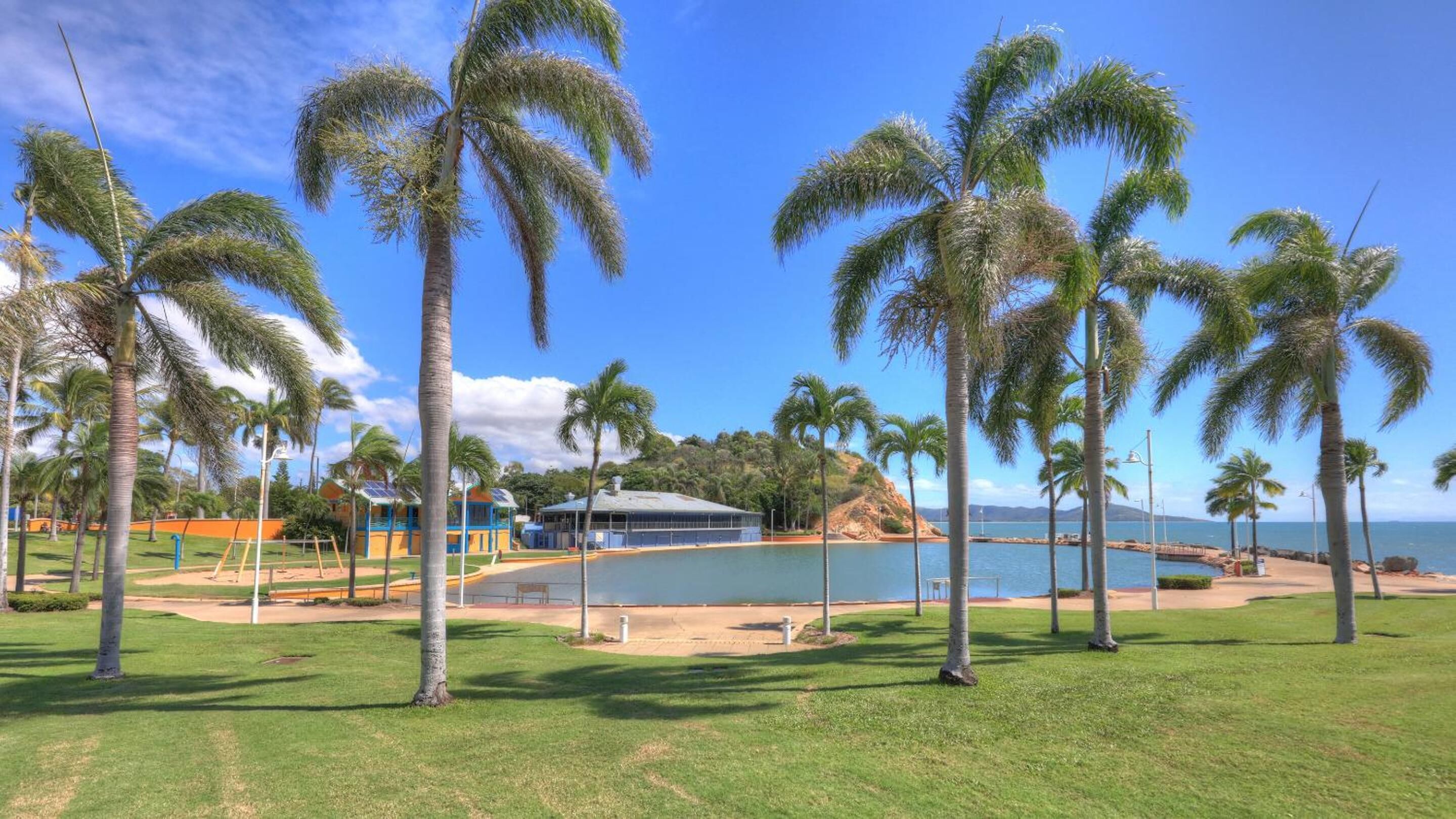 Una propiedad frente a la playa con palmeras, piscina y un edificio de techo azul.