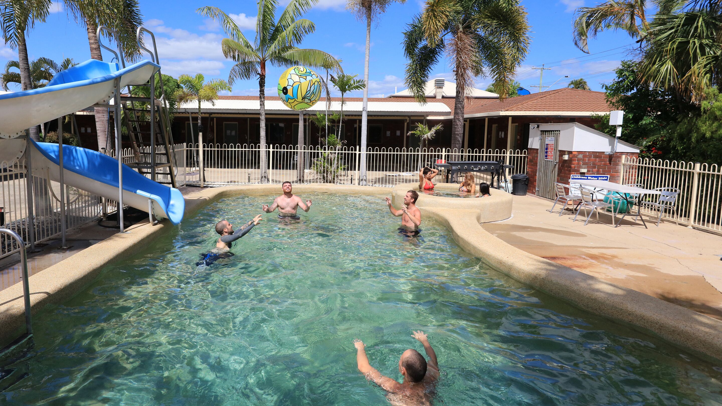 A swimming pool with a slide and palm trees in the background.