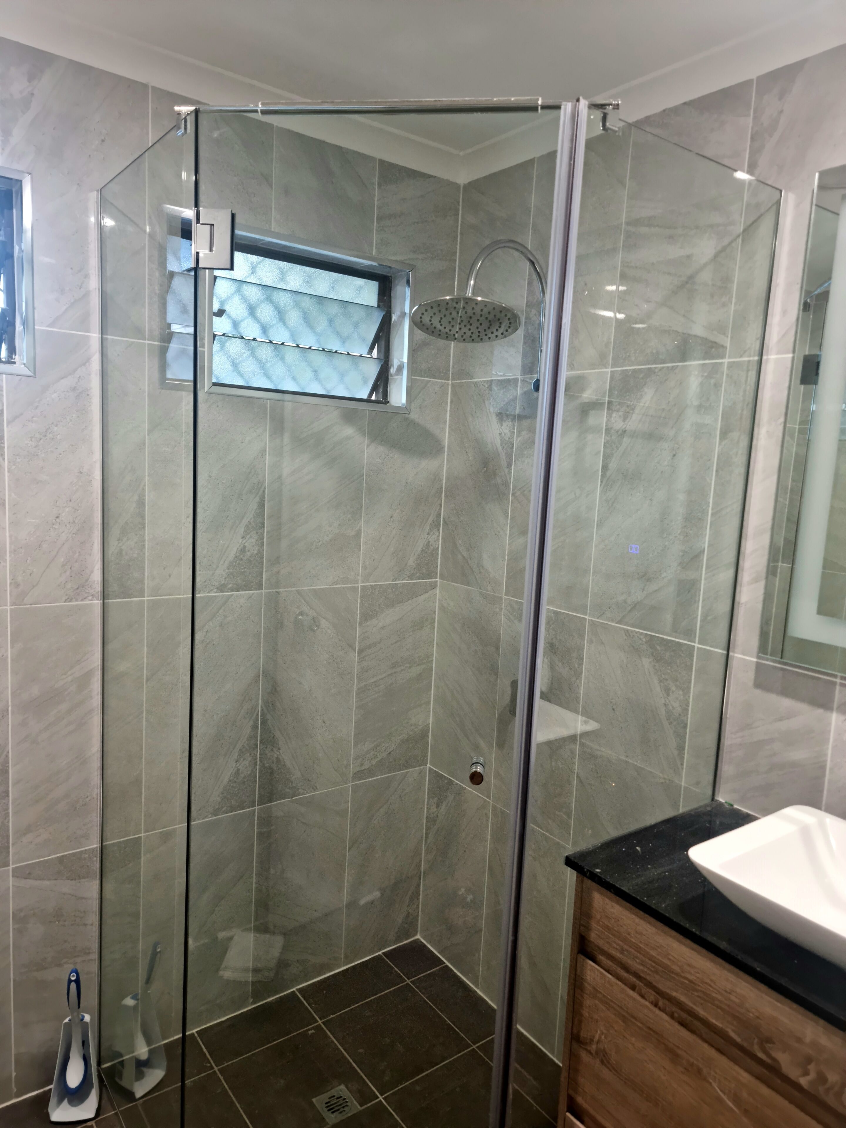 A modern bathroom with a glass-enclosed shower, a wooden vanity, and a large mirror.
