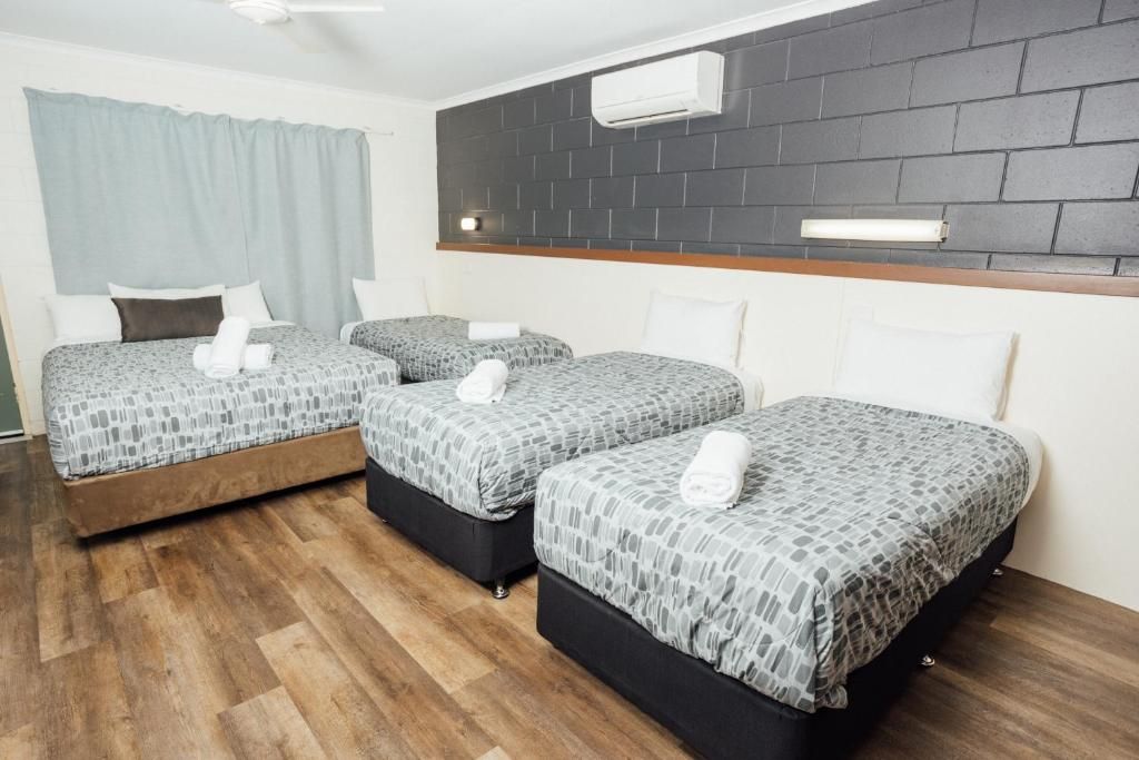 A hotel room with three beds, a wooden floor, a dark brick accent wall, and a ceiling fan.