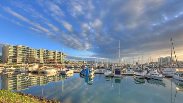 A marina with numerous boats docked, a large hotel building, and calm water reflecting the sky. - Billabong Lodge Motel (Rosslea)