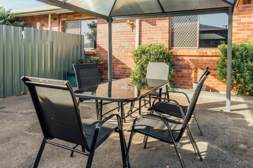 A covered outdoor patio with a table and chairs, a brick wall, and a metal fence.
