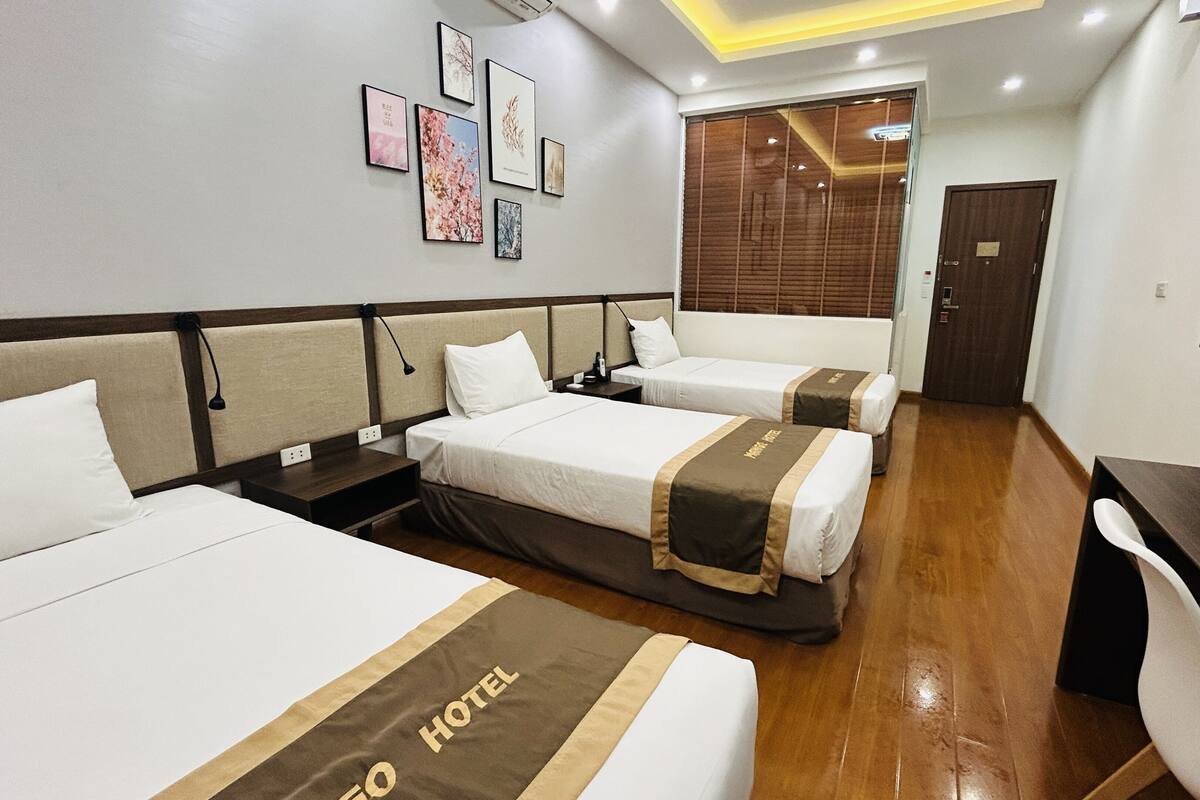 A hotel room with three beds, a TV, and a wooden floor.