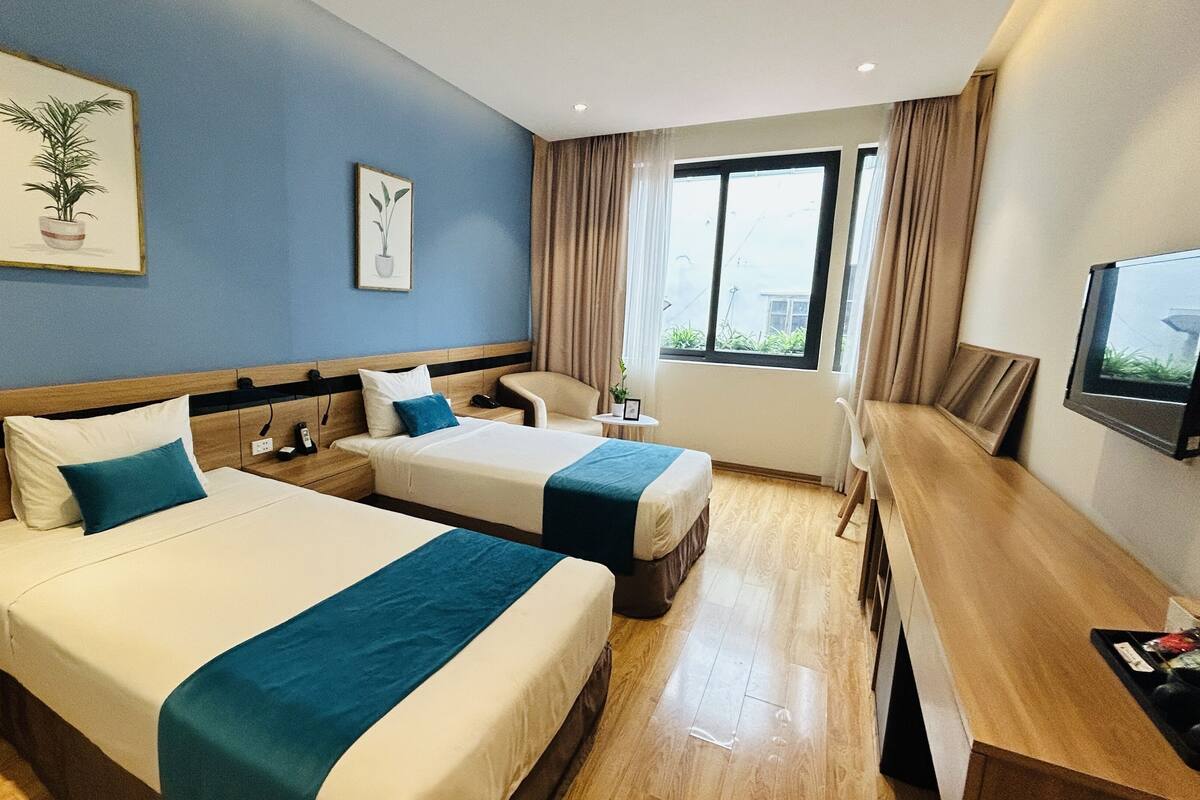 A hotel room with two beds, a desk, a chair, a TV, and a window with curtains.